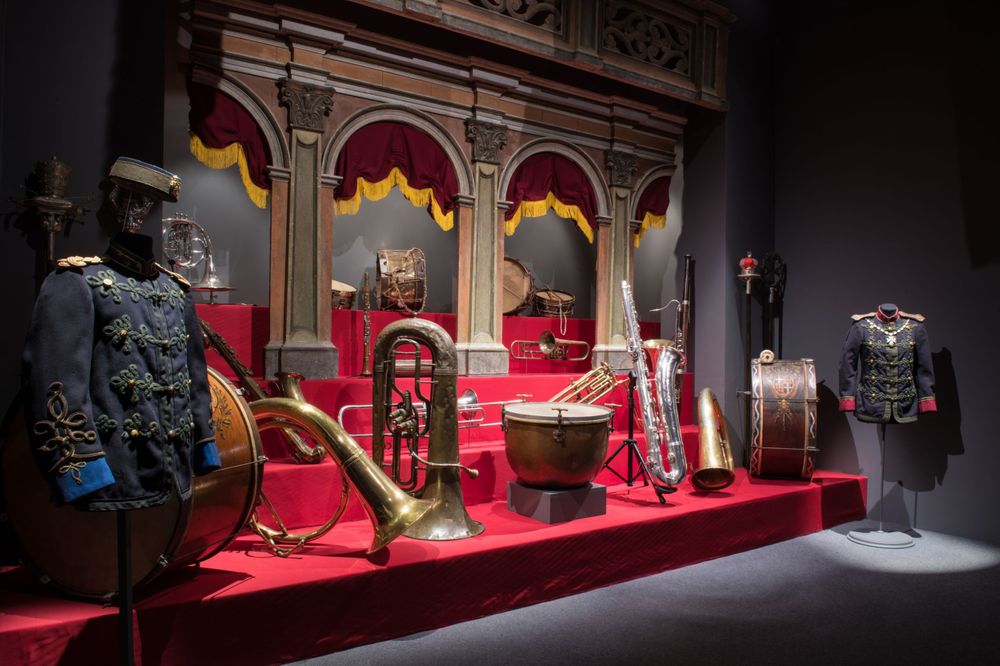 Ornate medieval thrones and royal artifacts displayed on red velvet in a museum exhibition.