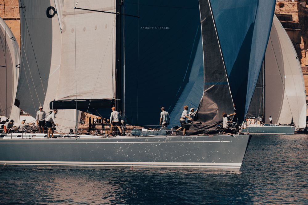 Close-up of racing sailboats competing on calm waters near a coastal town.