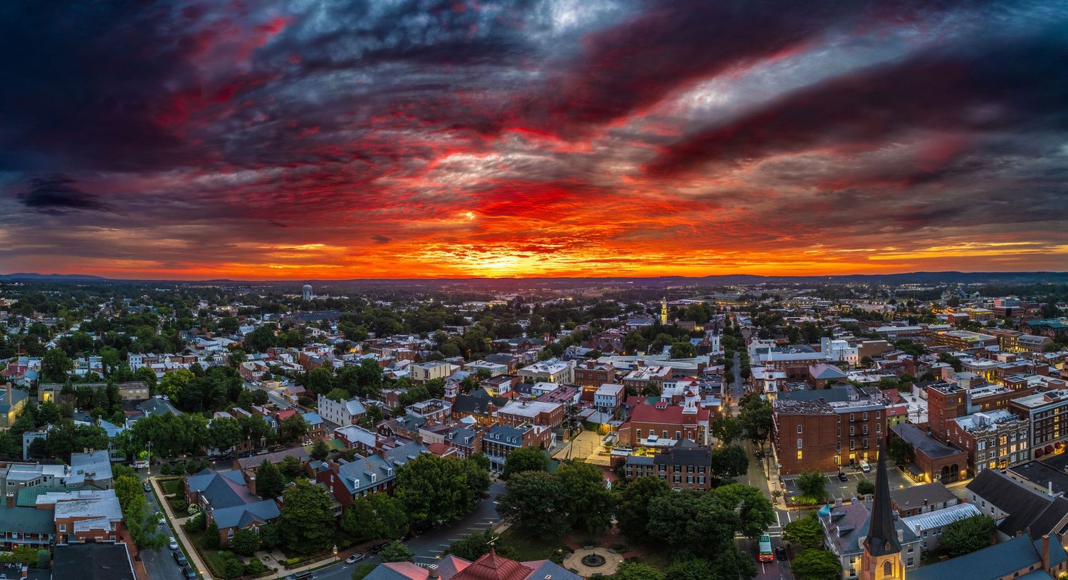 Dramatic sunset over a cityscape with red and orange clouds illuminating historic buildings and church spires.