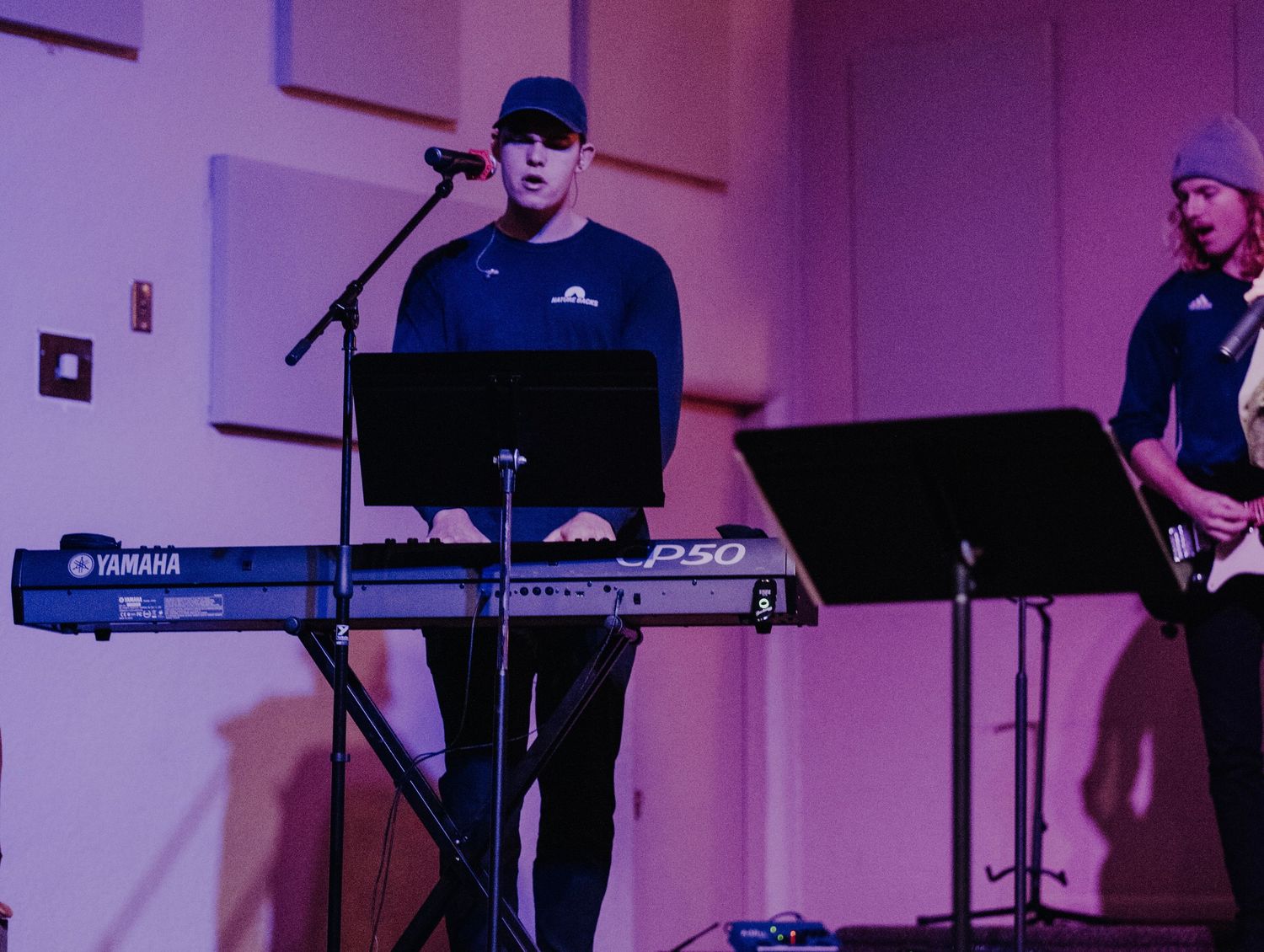 Musicians performing on stage with keyboard and instruments under purple lighting.