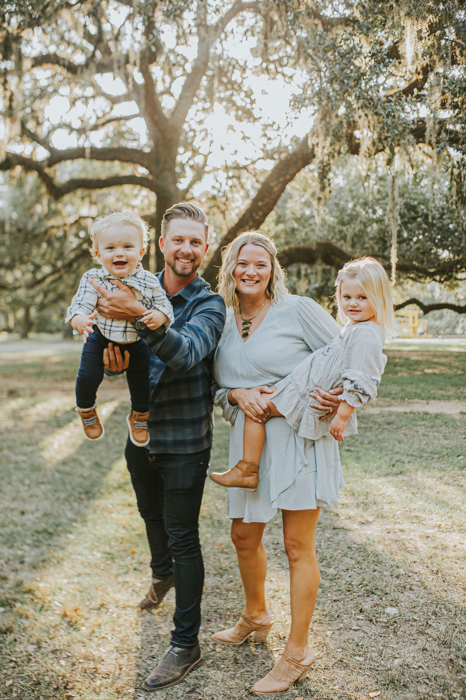 A family poses together outdoors under moss-draped trees in casual attire.