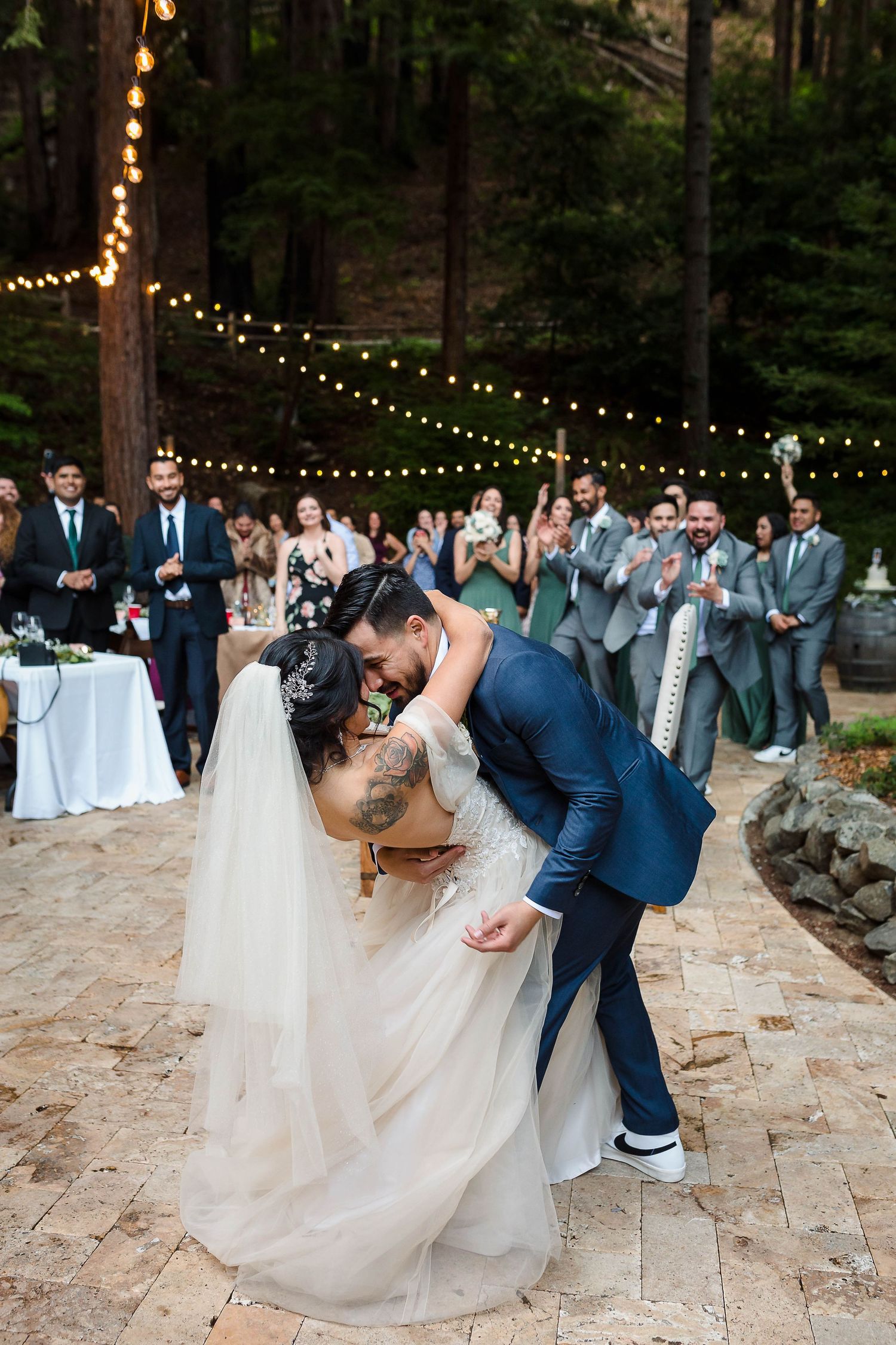Romantic outdoor wedding ceremony under string lights in a redwood forest setting.