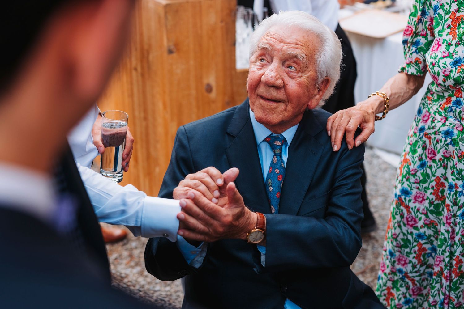An elderly guest enjoying conversations during an outdoor wedding reception.
