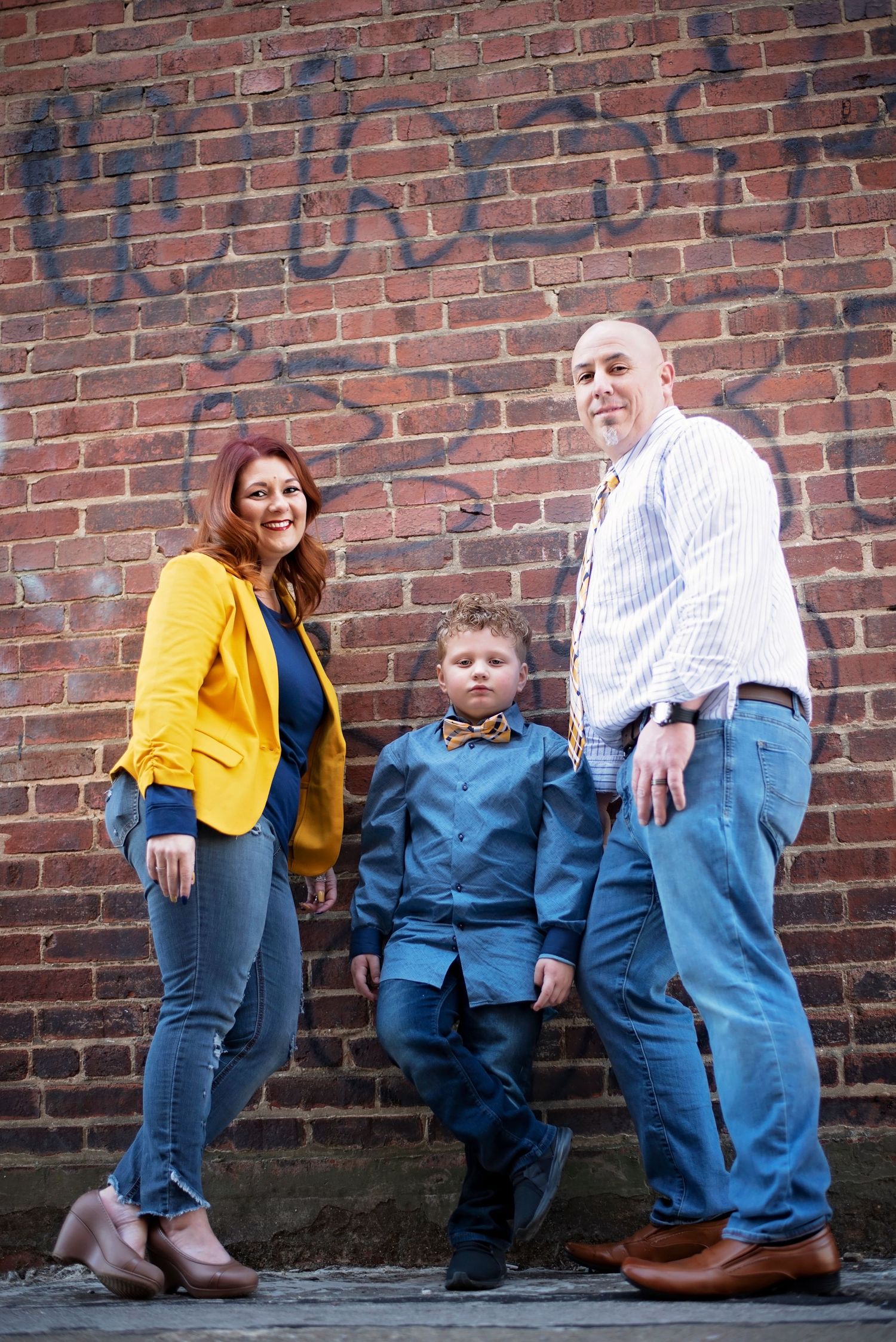 Family in coordinated outfits poses casually against brick wall.