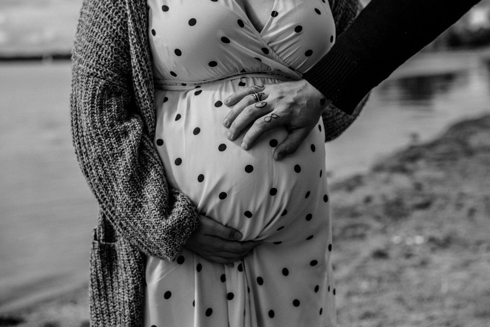 Seaside maternity photography with polka dot dress against moody water backdrop.