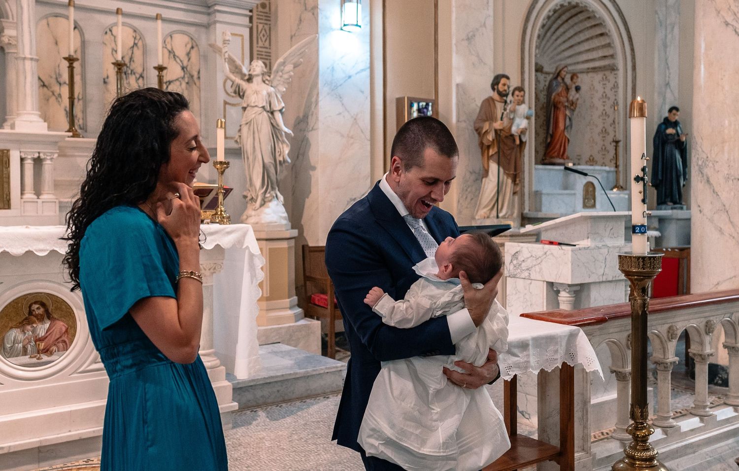Man smiling and holding baby dressed in white baptism gown at church