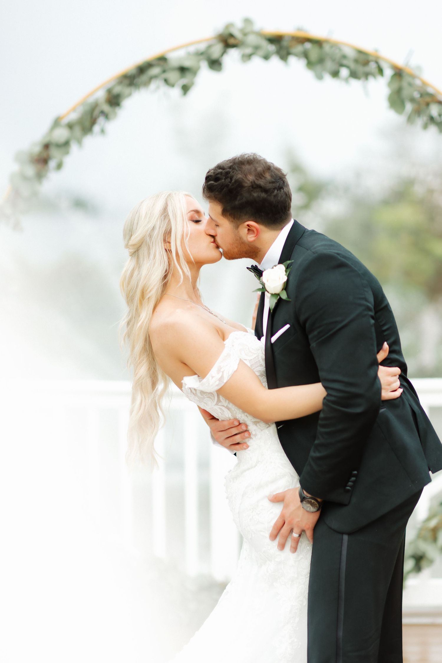 A romantic wedding moment under a floral arch with the couple sharing a tender kiss.