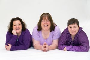 Three people in purple attire laying down for studio portrait on white background.