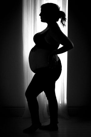 Artistic silhouette portrait highlighting pregnancy against backlit window.