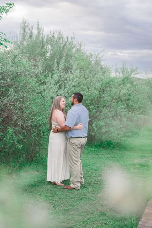 Romantic couple embracing in natural outdoor setting with green foliage.