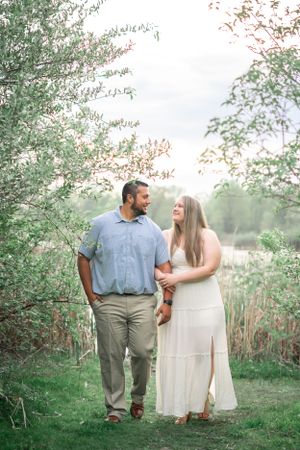 Couple walking hand in hand through lush garden pathway.