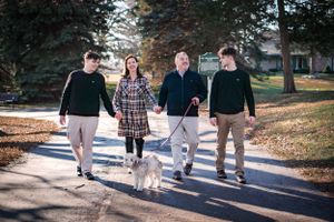 A group walks their fluffy white dog together on a path through an autumn park on a sunny day.