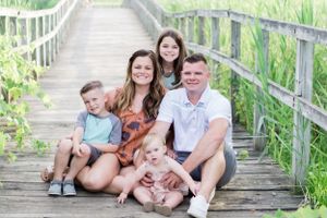 Family portrait session on wooden boardwalk surrounded by summer greenery.