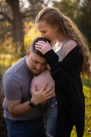 An intimate maternity moment captured outdoors during golden hour with natural backlighting.
