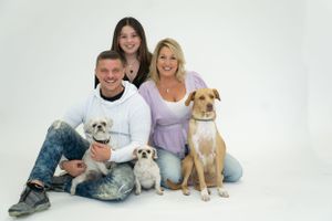 Family portrait with three dogs in a bright studio setting against white background.