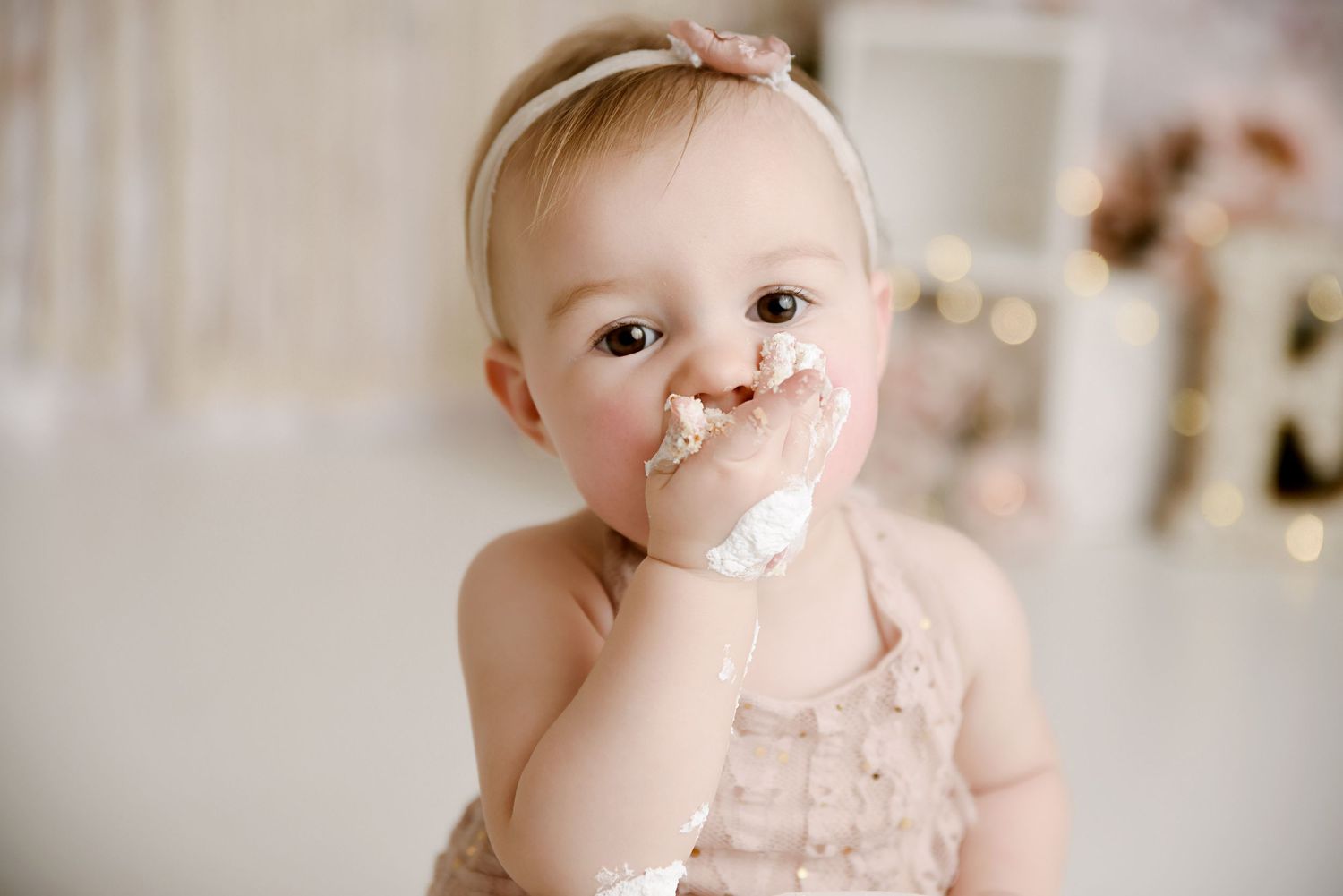 Adorable baby girl with cake on her face during first birthday cake smash in pink ruffled outfit.