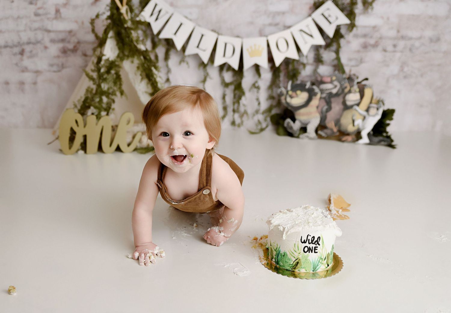 Red-haired baby boy crawls toward Wild One themed smash cake during first birthday photo session.
