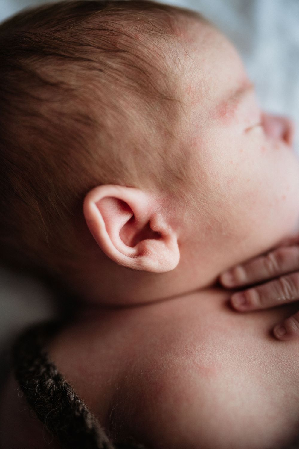 Macro detail shot of newborn baby's ear and soft skin in gentle lighting.