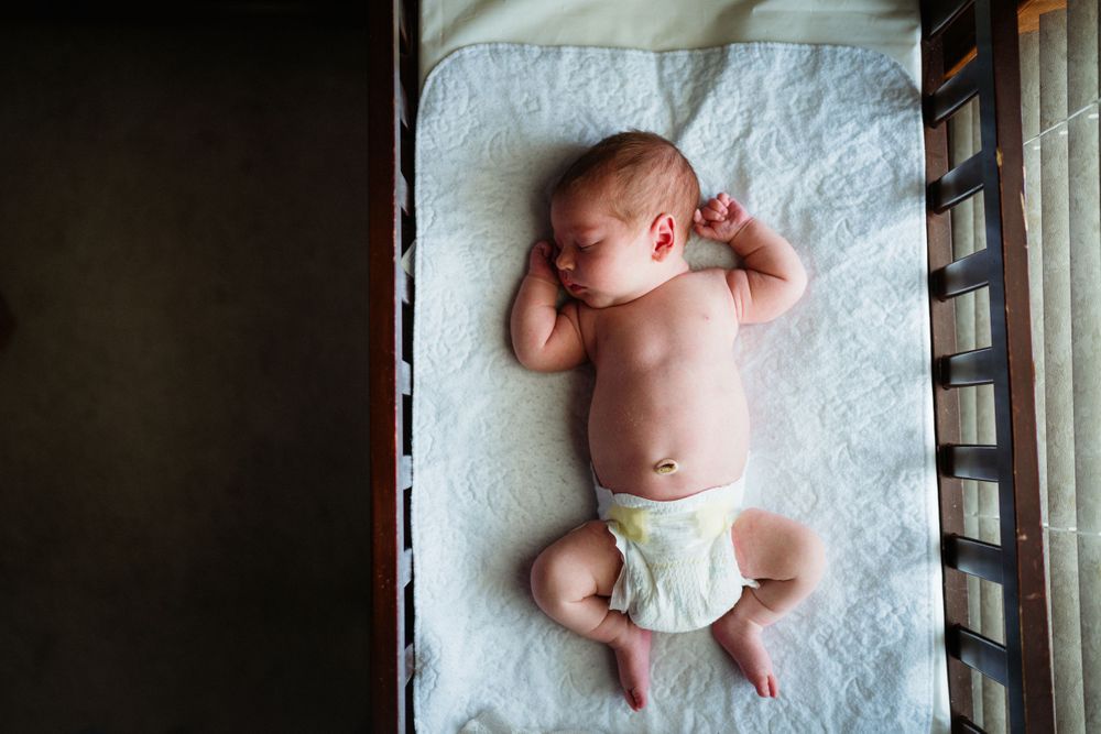 Overhead view of sleeping newborn baby in white diaper on crisp white bedding.