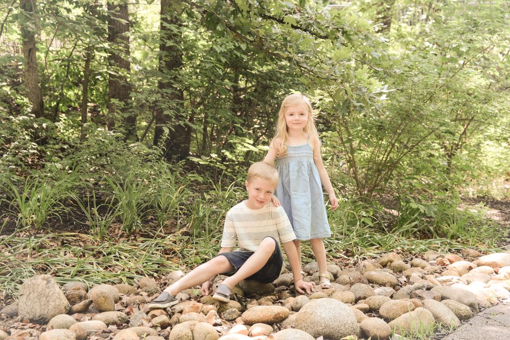 Two children sitting on rocky riverbed in woodland setting.