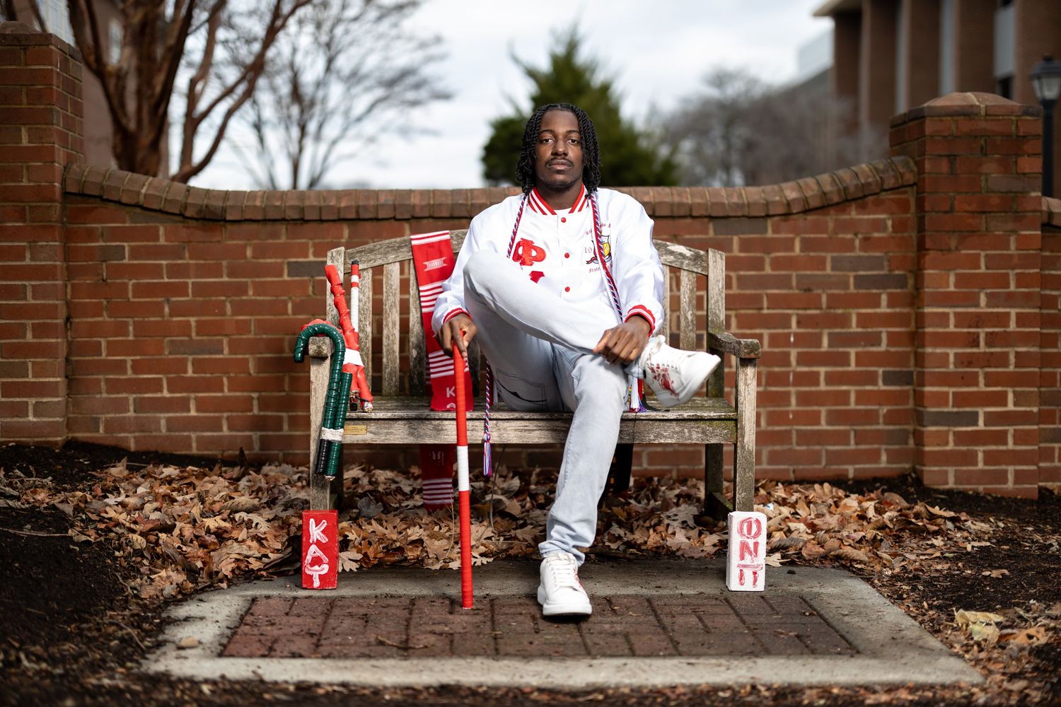 Graduate in all-white outfit relaxing on outdoor bench with decorative elements.