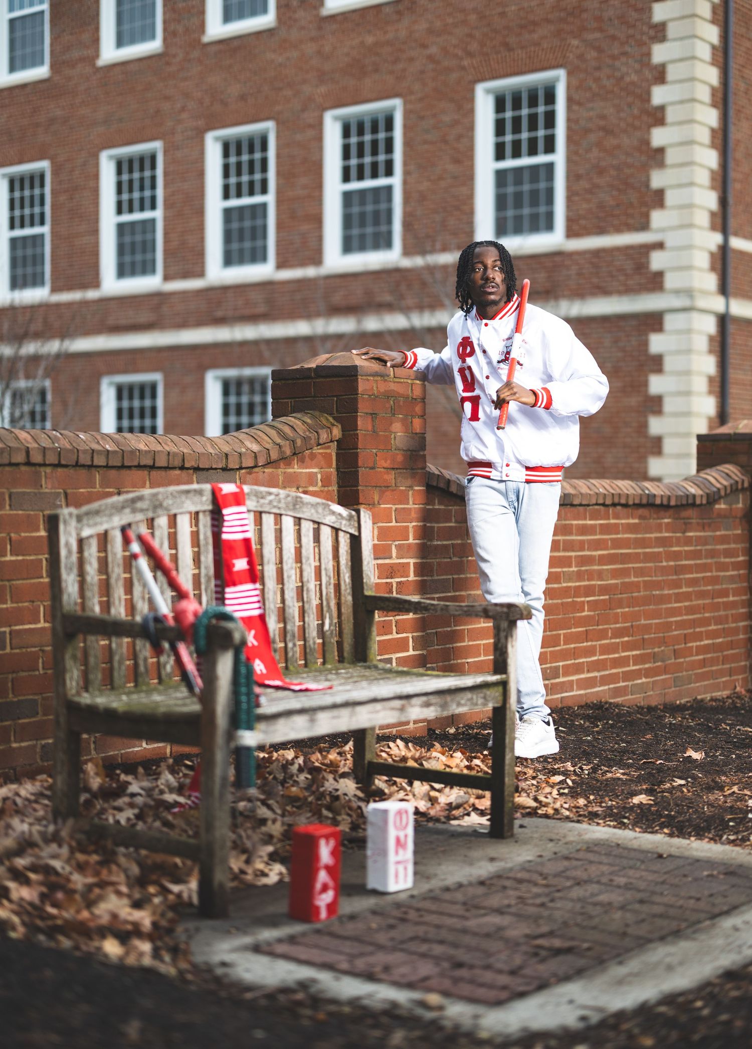 Graduate in white athletic wear standing near brick wall and bench on campus.