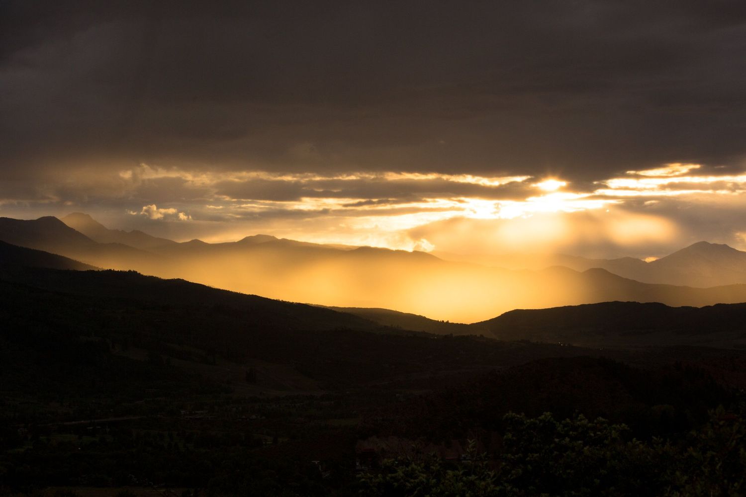 Dramatic sunset over mountain peaks with sunbeams breaking through dark clouds.