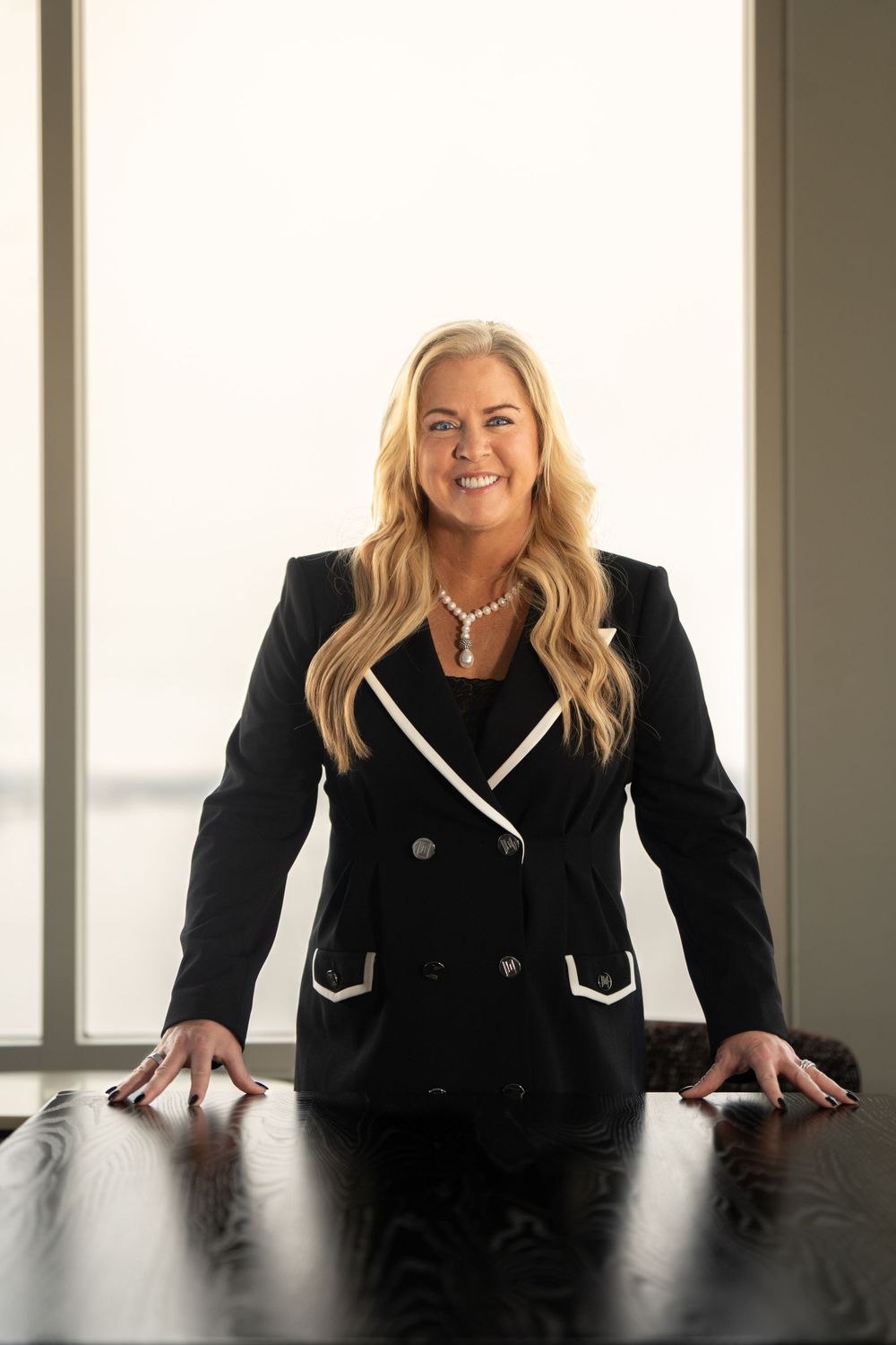 Executive in black blazer with white trim standing confidently at dark conference table. Quad Cities Business Headshot Photography