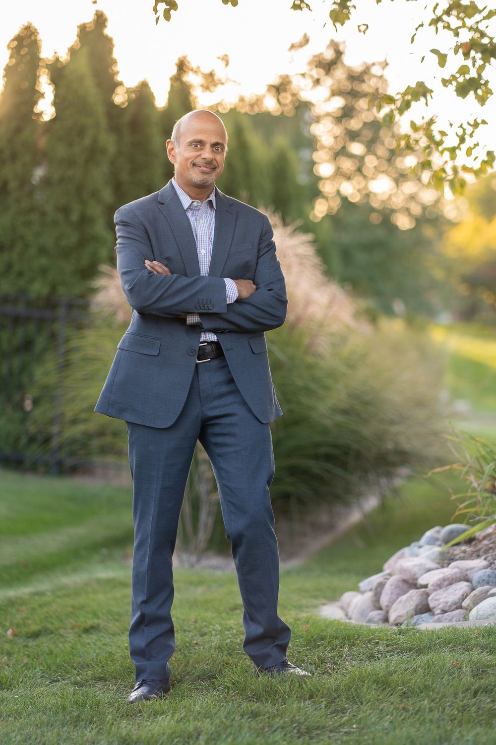 Professional in navy suit standing outdoors at sunset with landscaped garden background. Quad Cities Business Headshot Photography