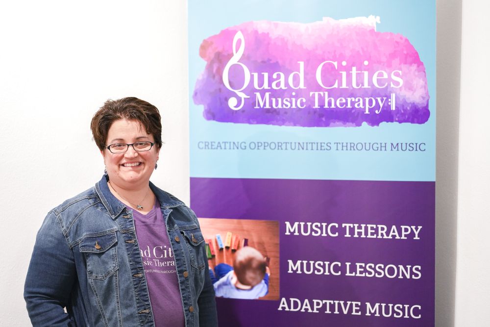 Music therapist standing in front of Quad Cities Music Therapy banner wearing denim jacket. Quad Cities Business Headshot Photography