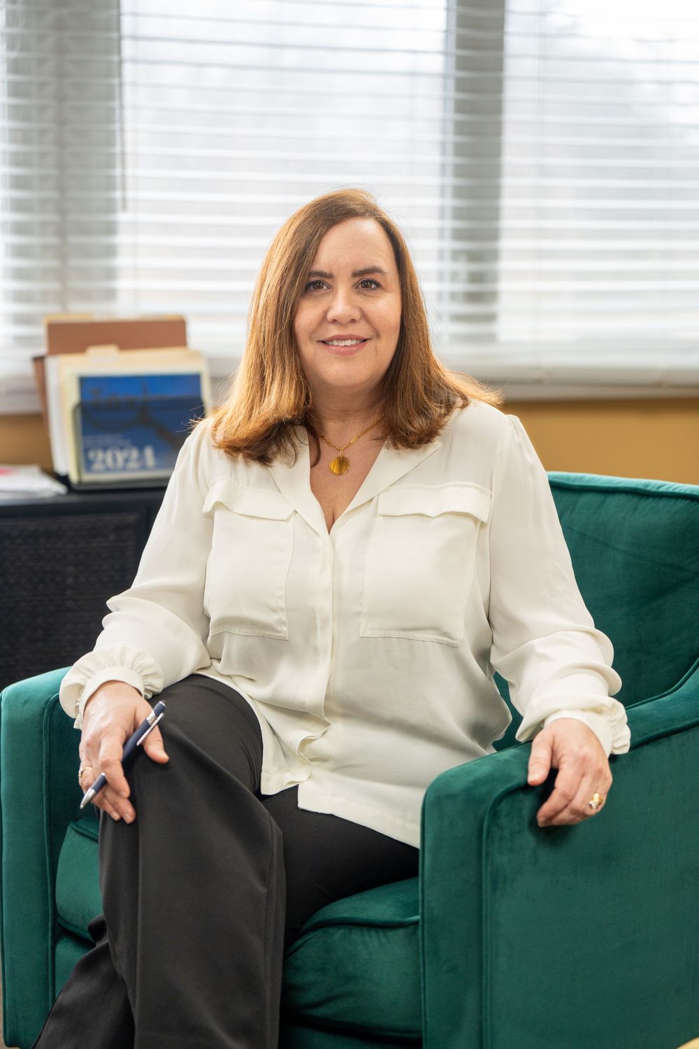 Professional seated in emerald green armchair wearing cream colored blouse in bright office space. Quad Cities Business Headshot Photography