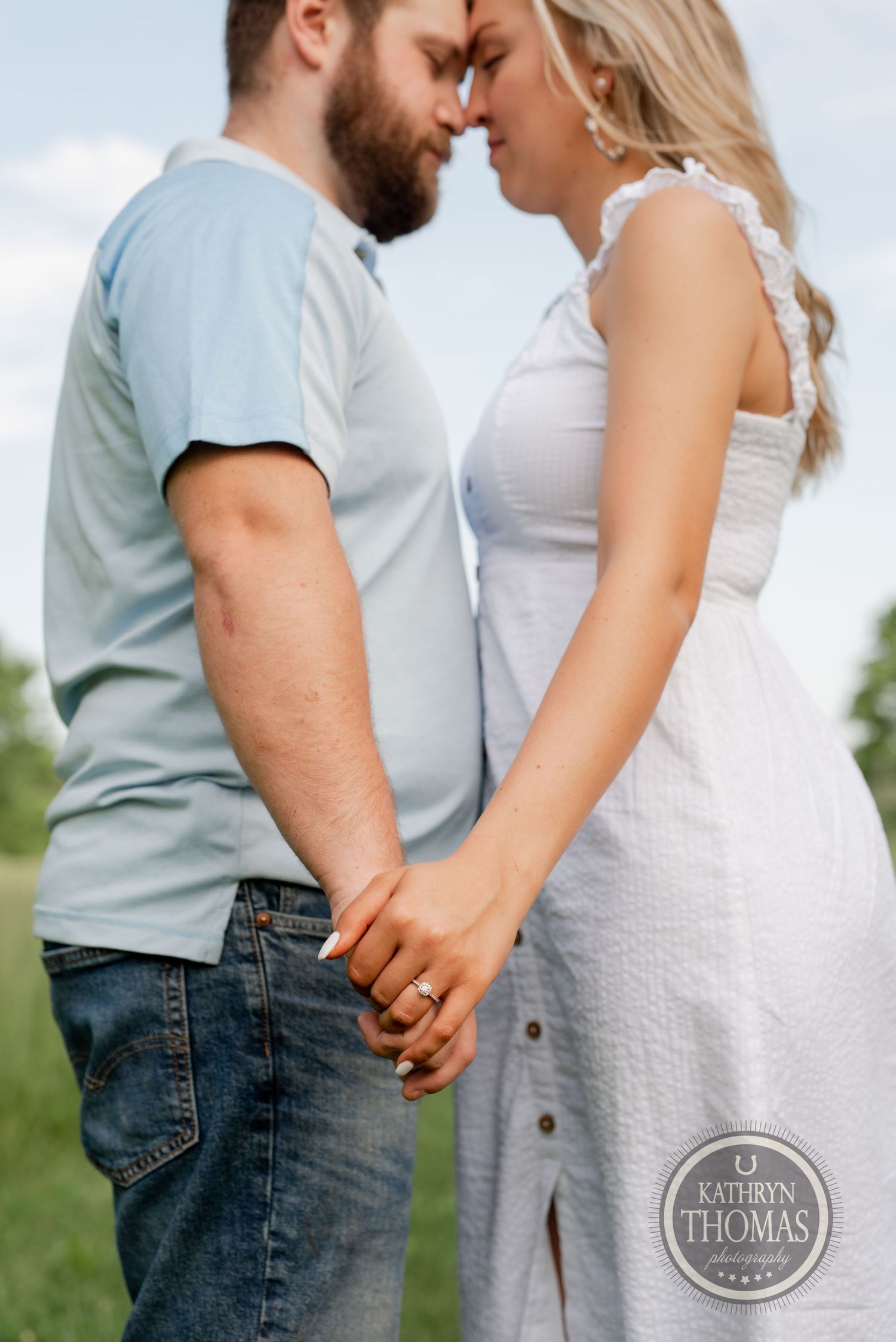 Tender moment between a couple holding hands in a sun-lit field wearing casual summer attire.