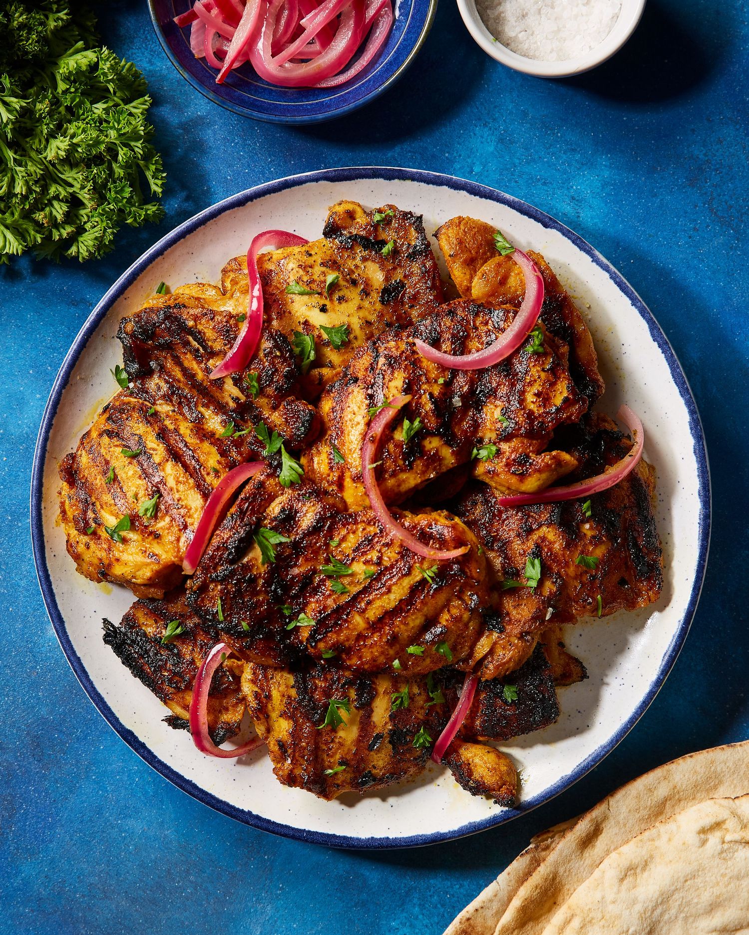 Tandoori chicken with red onions and fresh herbs served on white plates against a dark blue background.