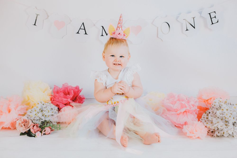 First birthday cake smash session with pink decorations and banner against white background.