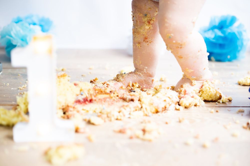 Close-up of tiny feet and scattered cake crumbs on wooden floor with blue decorations.