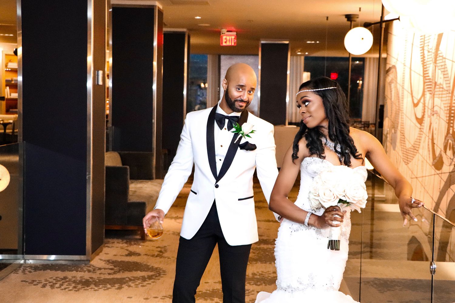 Couple in formal attire shares a celebratory dance moment in a hotel hallway.