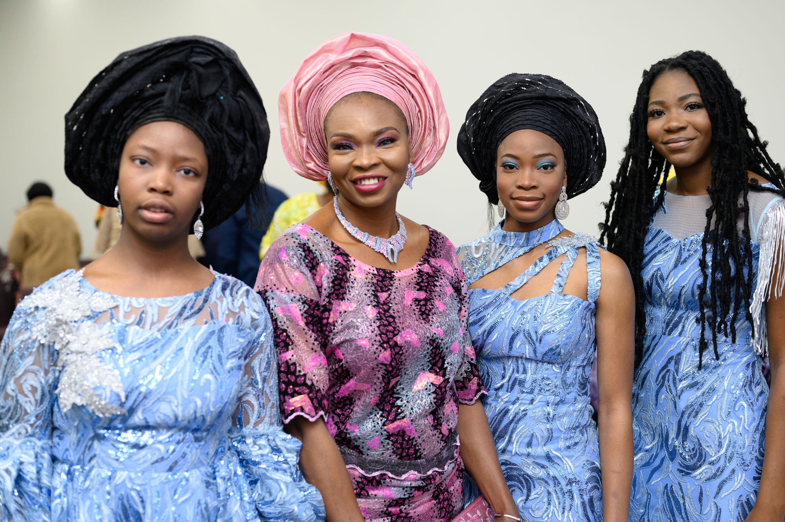 Group portrait of women in coordinated blue dresses and traditional headwraps at formal event.