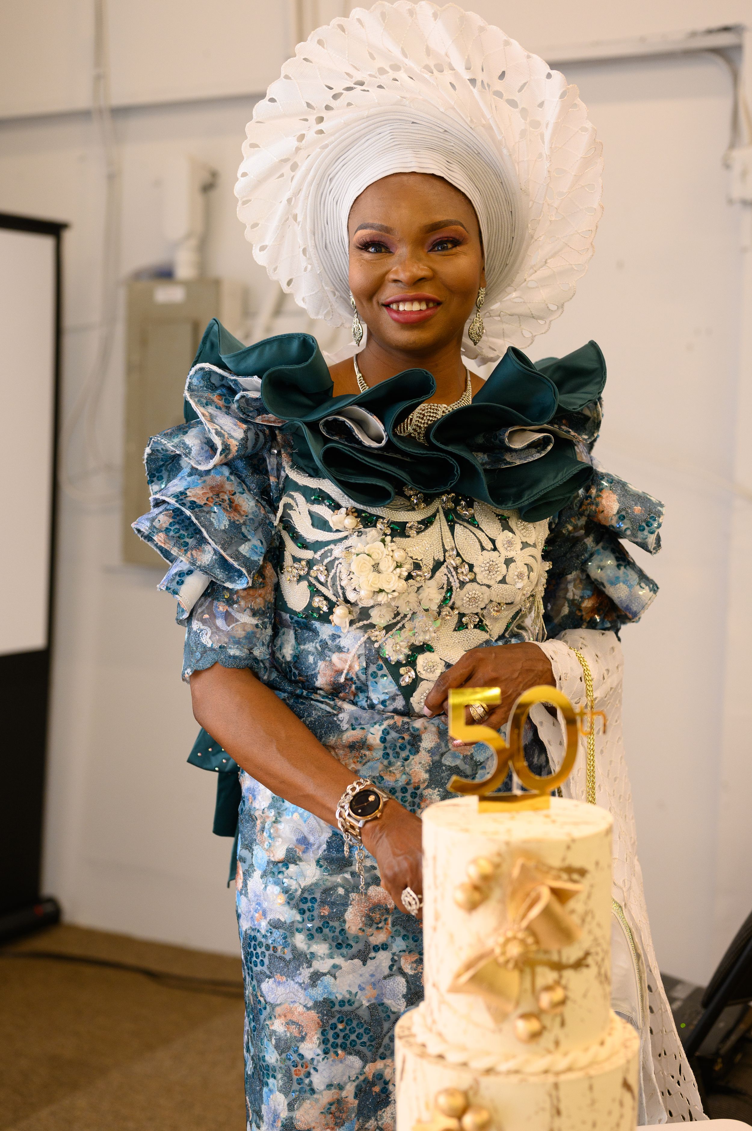 Traditional African wedding attire featuring a blue floral dress with ruffled details and white gele headpiece.