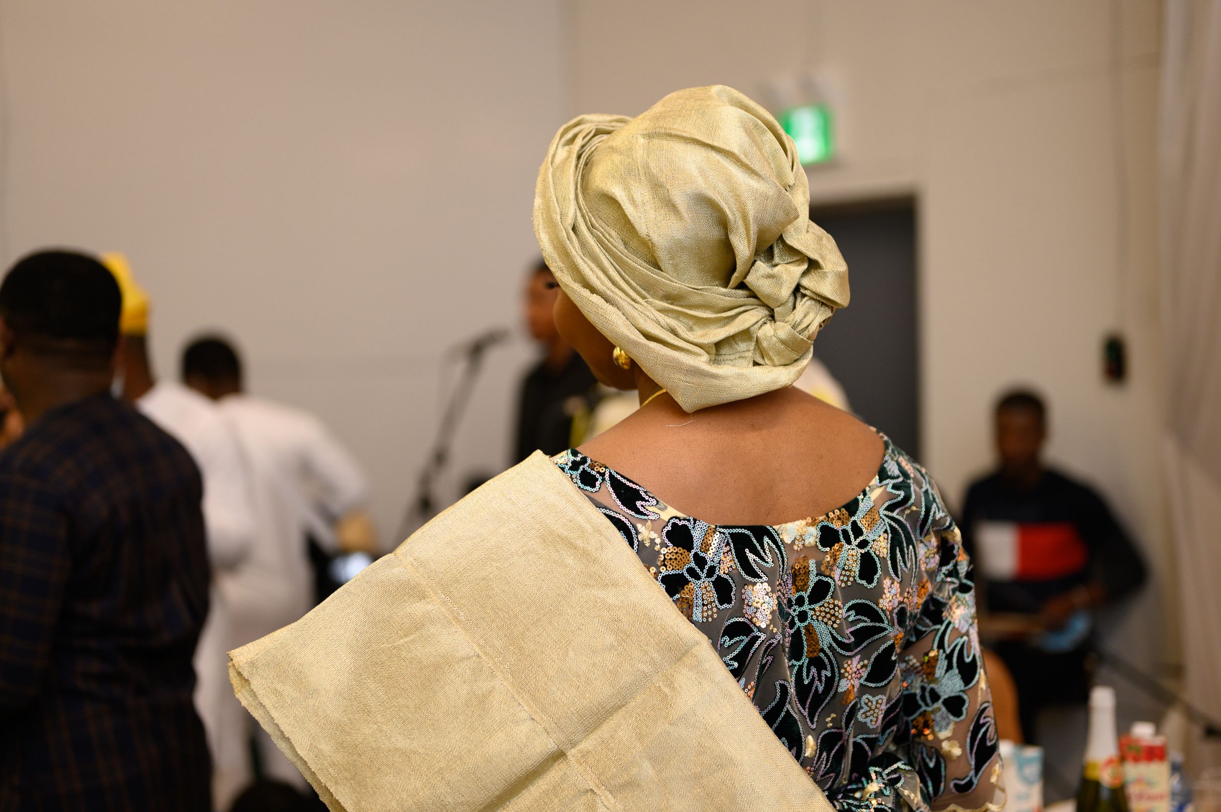 Person wearing traditional headwrap and patterned clothing at formal gathering.