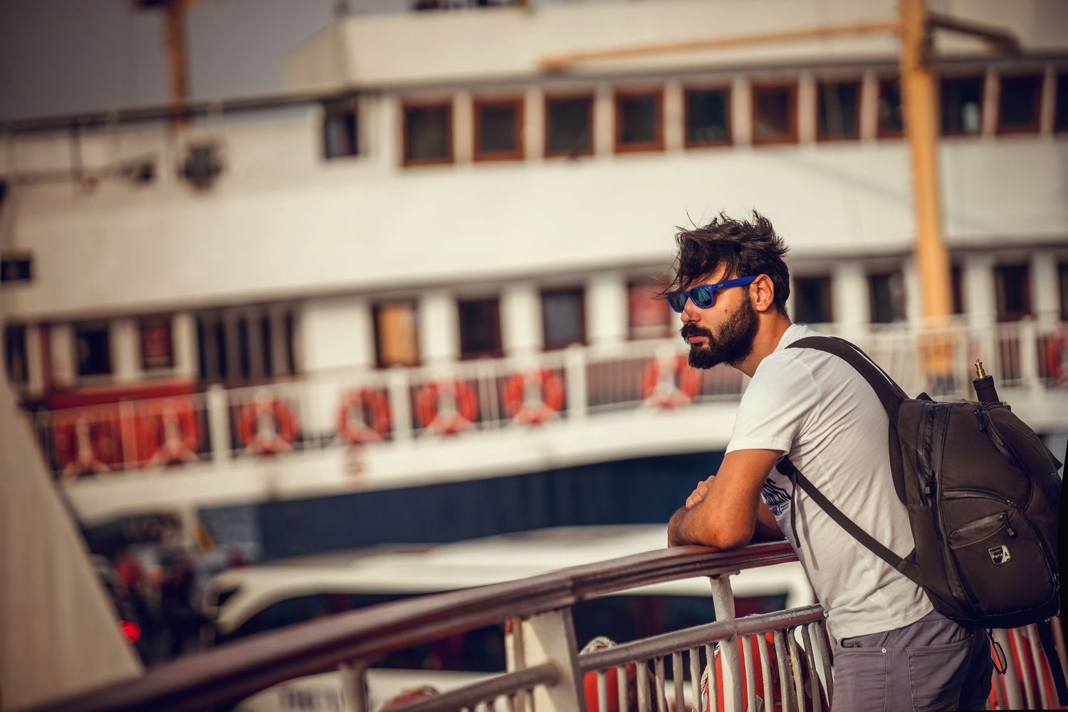 Man with backpack and sunglasses looking out from boat or ferry deck.