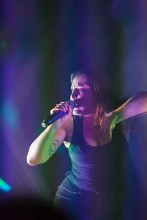 Dramatic concert scene with performer in tank top illuminated by purple and blue stage lights.