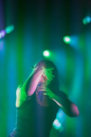Expressive performance moment captured under moody teal and green stage lighting.