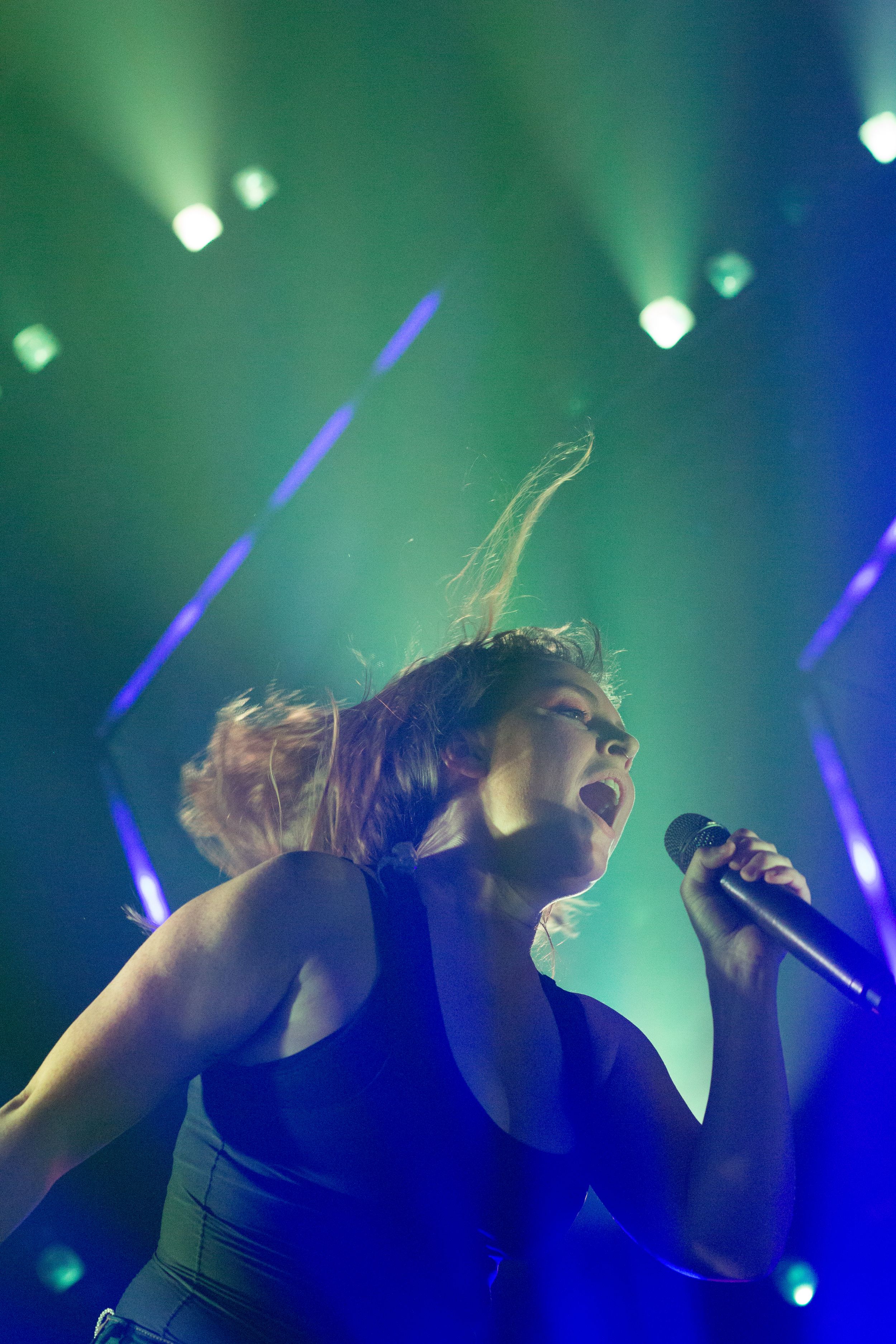 A performer moves energetically under blue and green stage lighting.