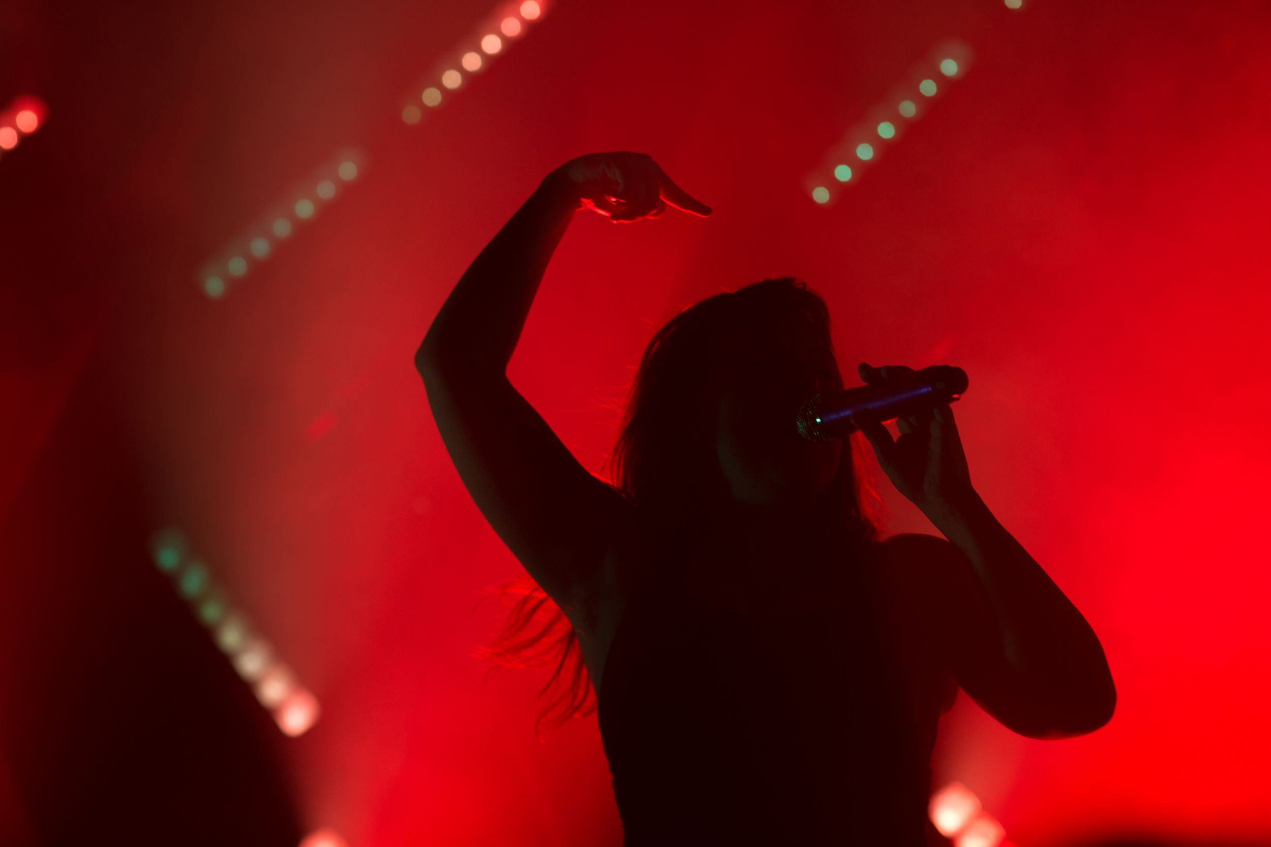 A performer is silhouetted against intense red stage lighting and LED displays.