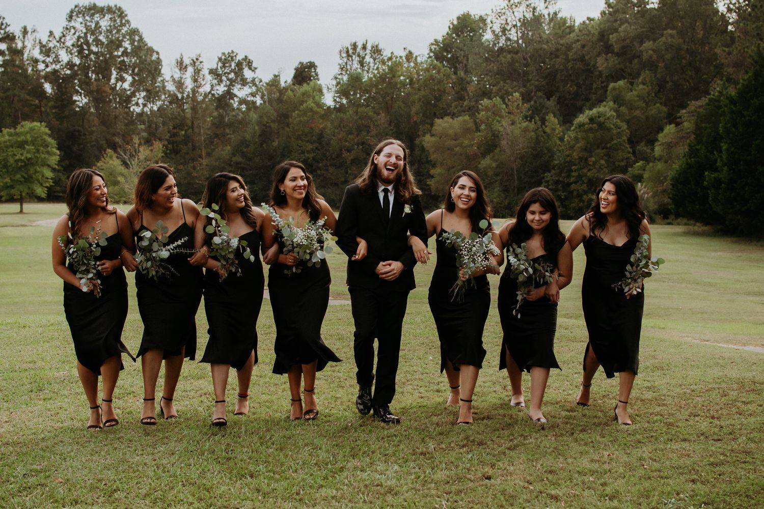 Wedding party walking and laughing together across a green field.