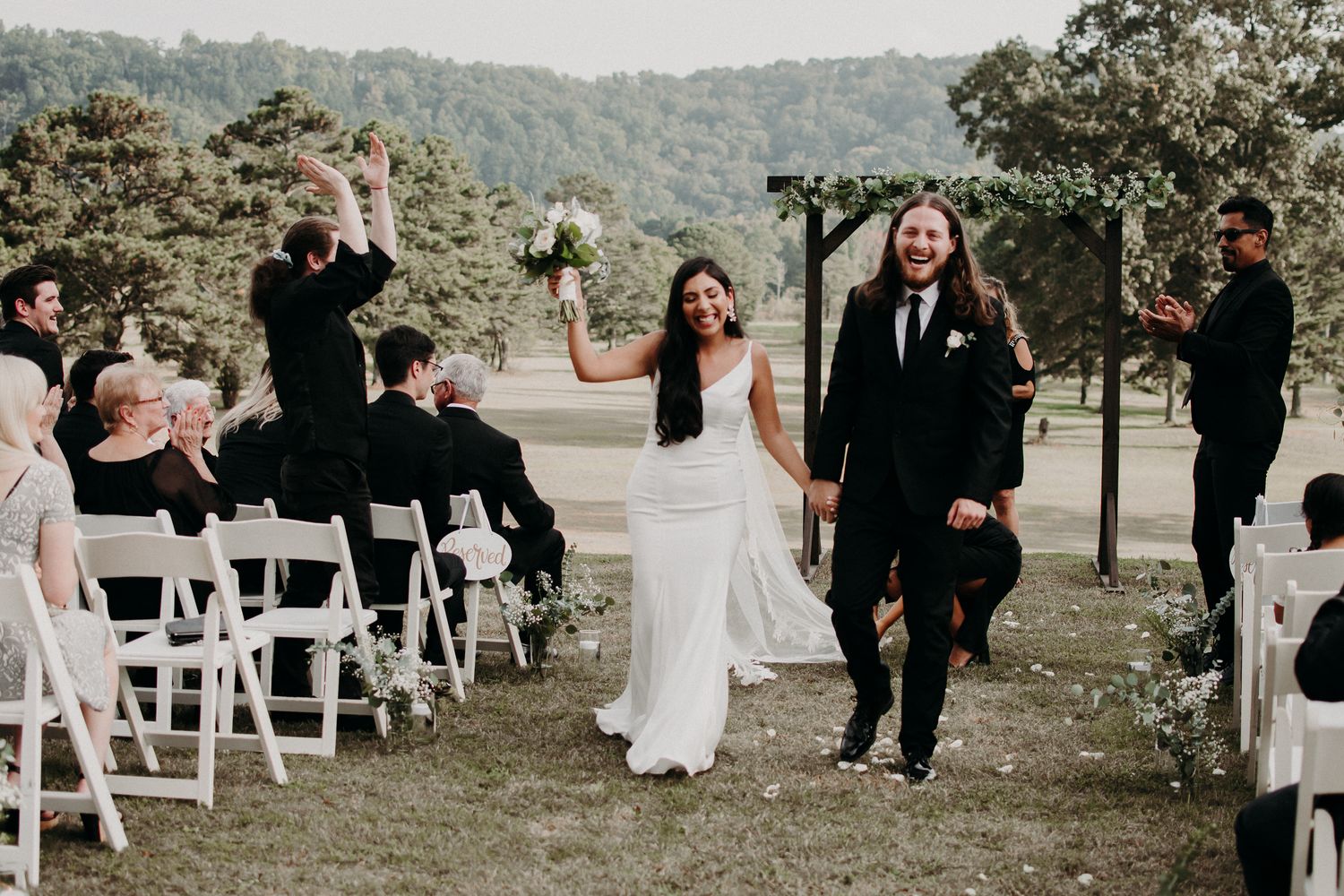 Newlyweds exit their outdoor ceremony while guests celebrate with sparklers.