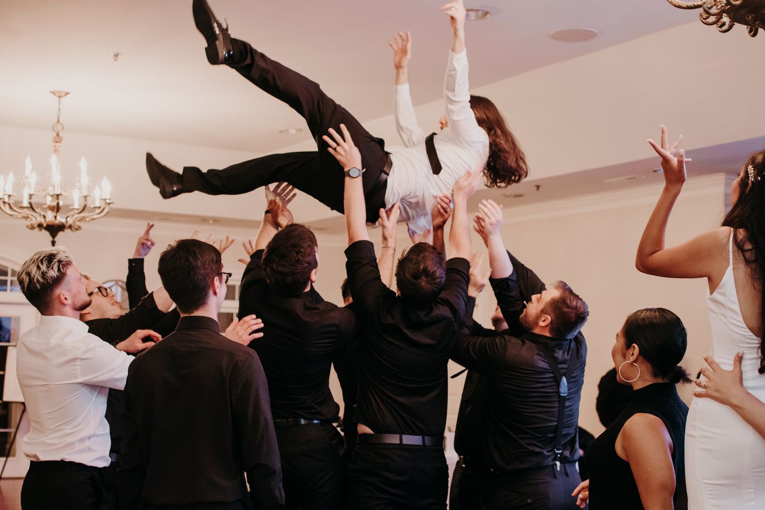Wedding guests lift and toss celebrants during reception dance party.