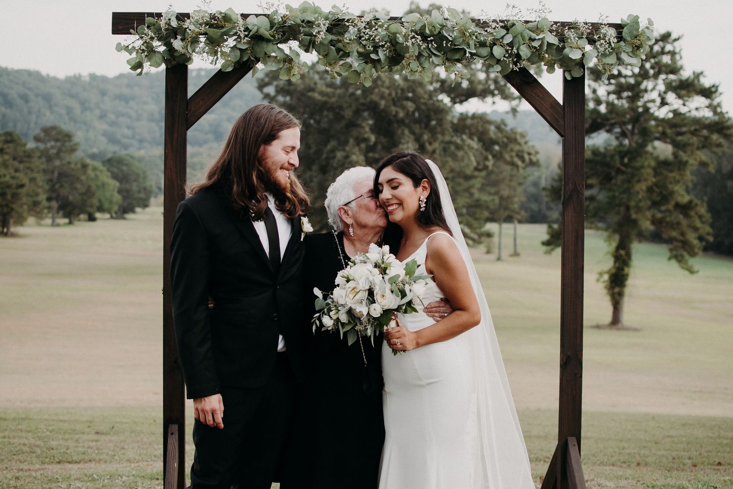 An emotional wedding moment captured under a green-decorated wooden arch.