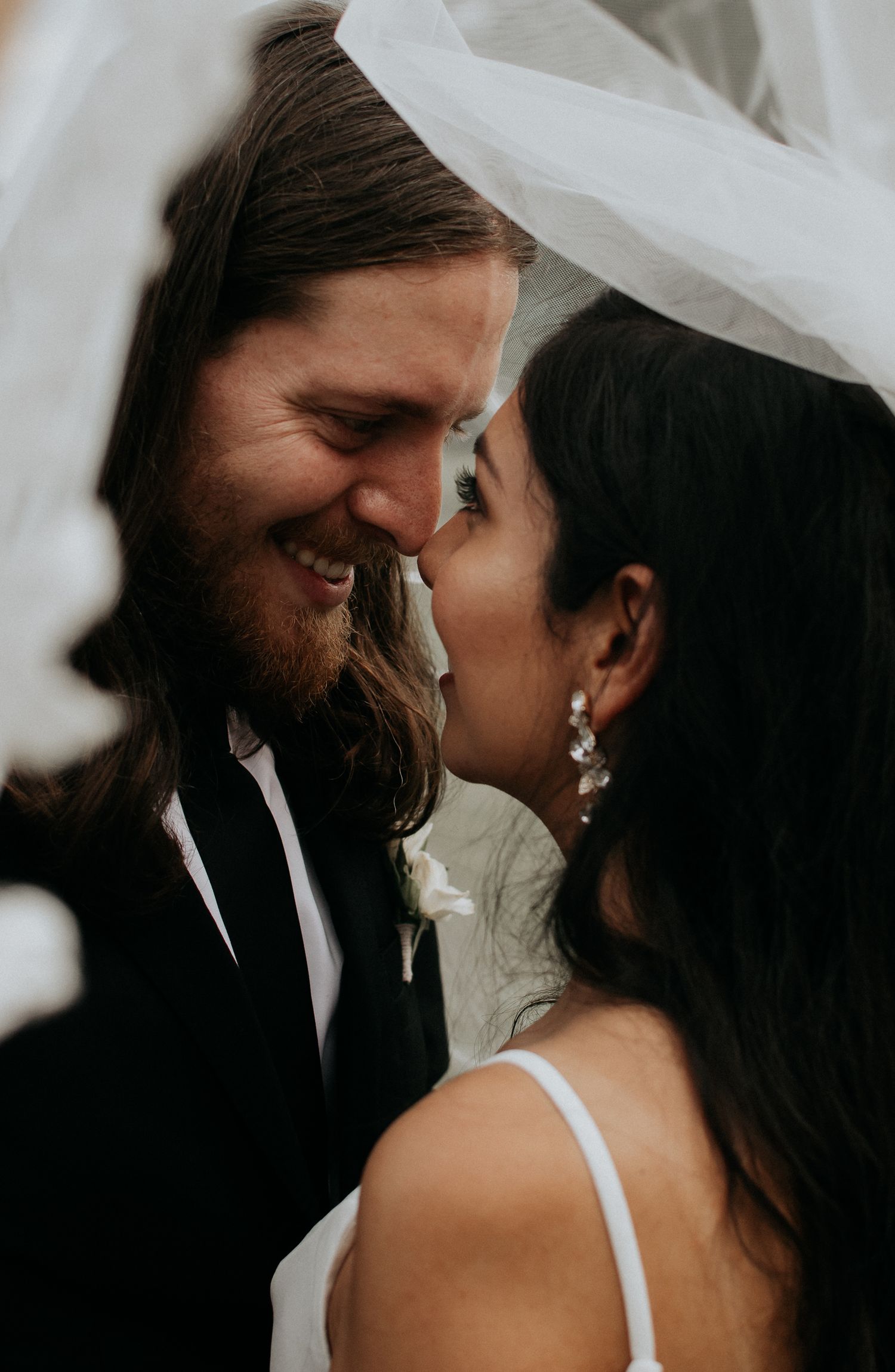 Intimate close-up of couple sharing a tender moment under a wedding veil.