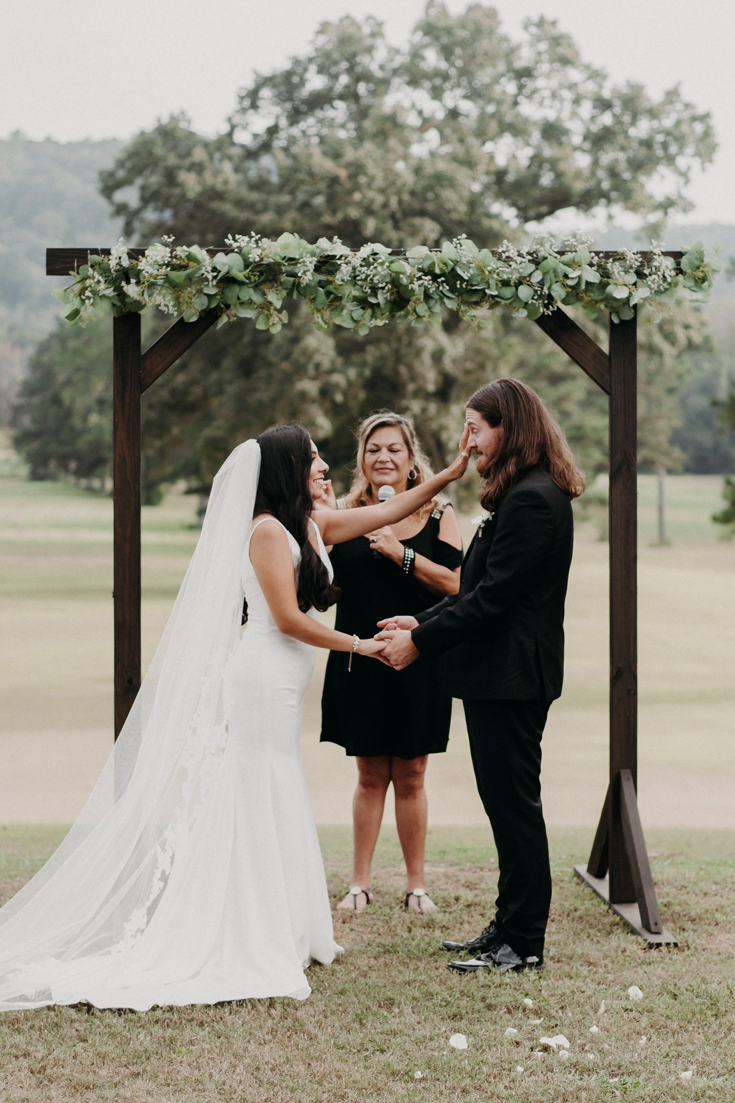 A wedding ceremony under a floral-adorned wooden arch with an officiant and couple.